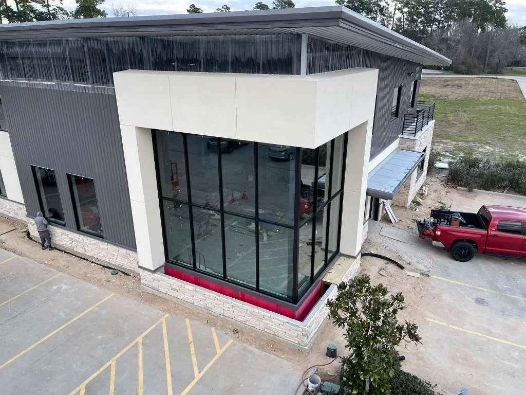 A modern commercial or office building with large glass windows installed by Glassworks, dark and white exterior walls, and a parking lot with yellow striped spaces.
