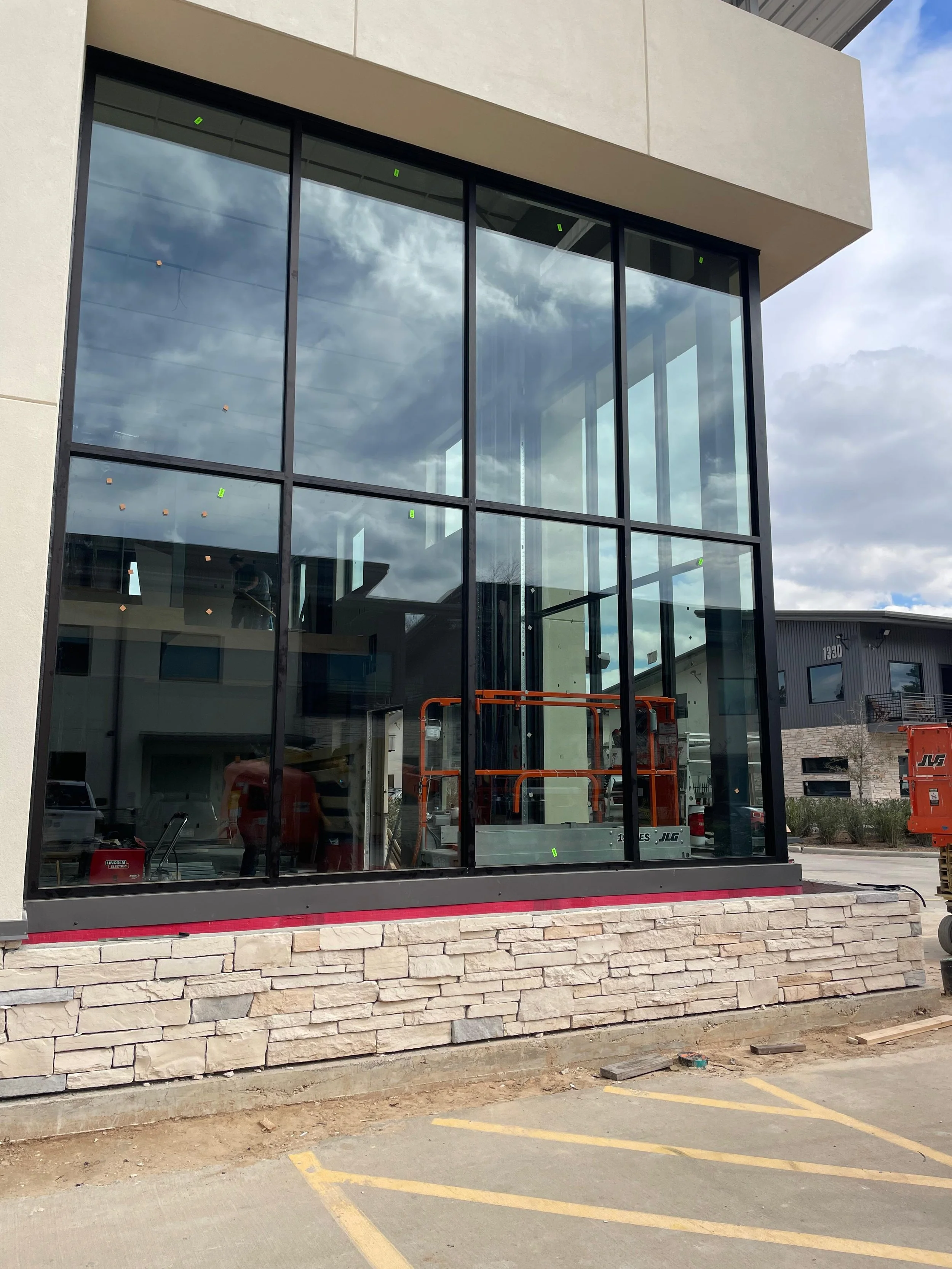 Construction site featuring a building with large glass windows installed by Glassworks, stone veneer on the lower part of the exterior wall, and construction equipment inside and outside.