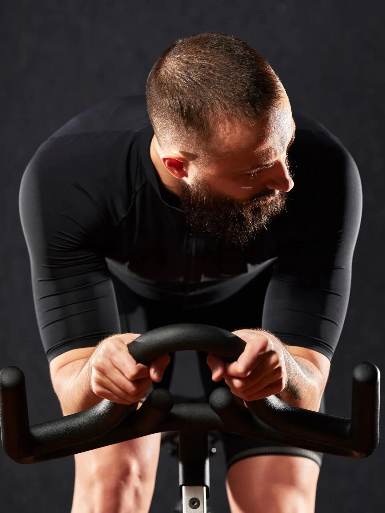 man-exercising-on-stationary-bike-in-dark-room-2026-03-17-17-12-17-utc.jpg