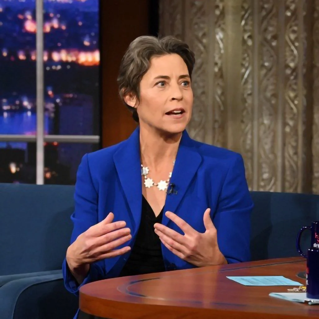 Maria J Stephan in a blue blazer sitting and speaking with hand gestures on the Colbert Show