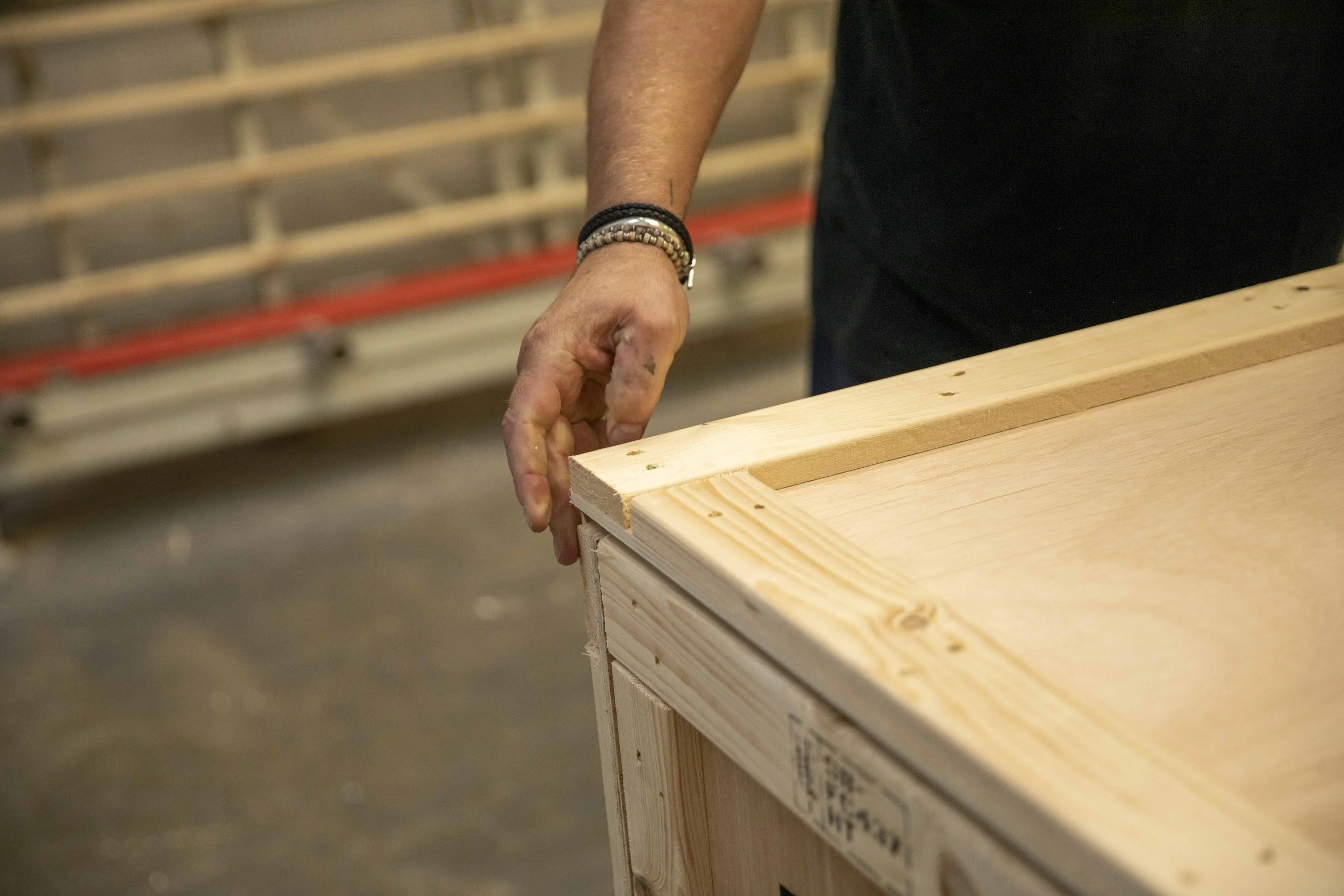 Mani soulevant le coin d'une grande planche de bois dans un atelier.