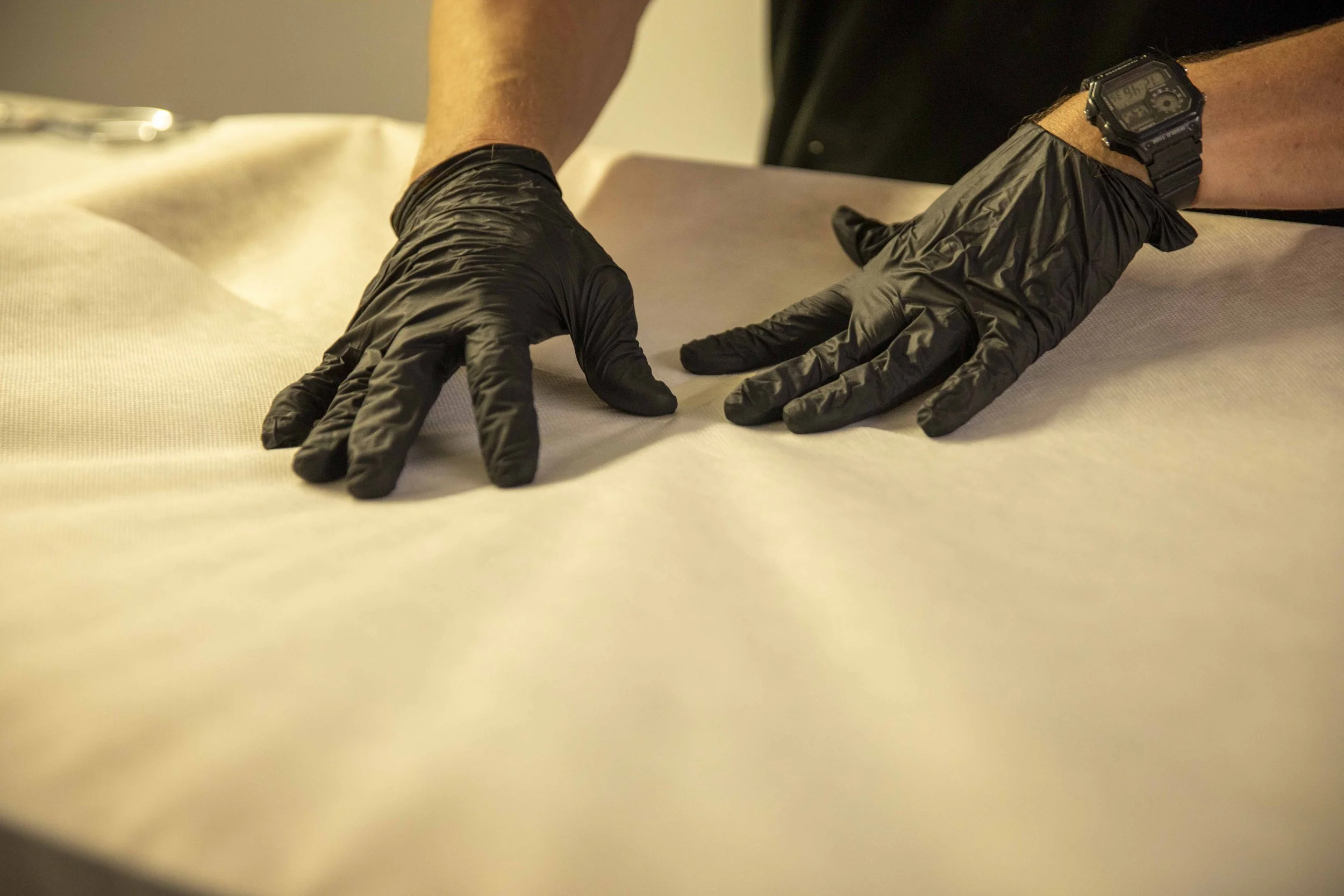 Mains portant des gants noirs étalant une couche de papier ou de tissu sur une surface plane.