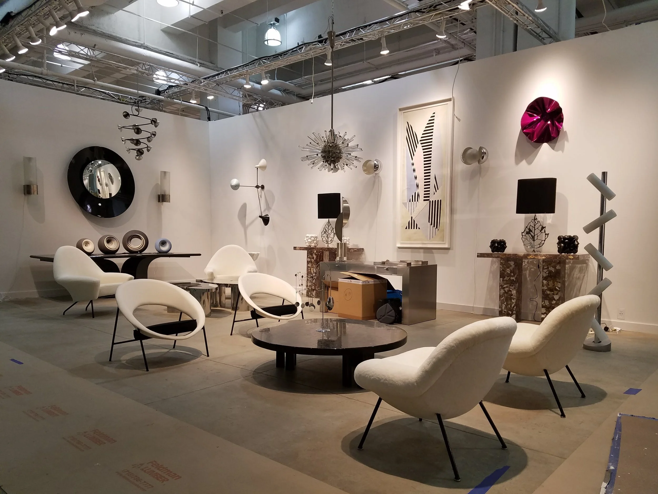 Une salle d'exposition de meubles modernes avec des fauteuils blanc, des tables basses noires, et des décorations artistiques murales, dans un espace bien éclairé.