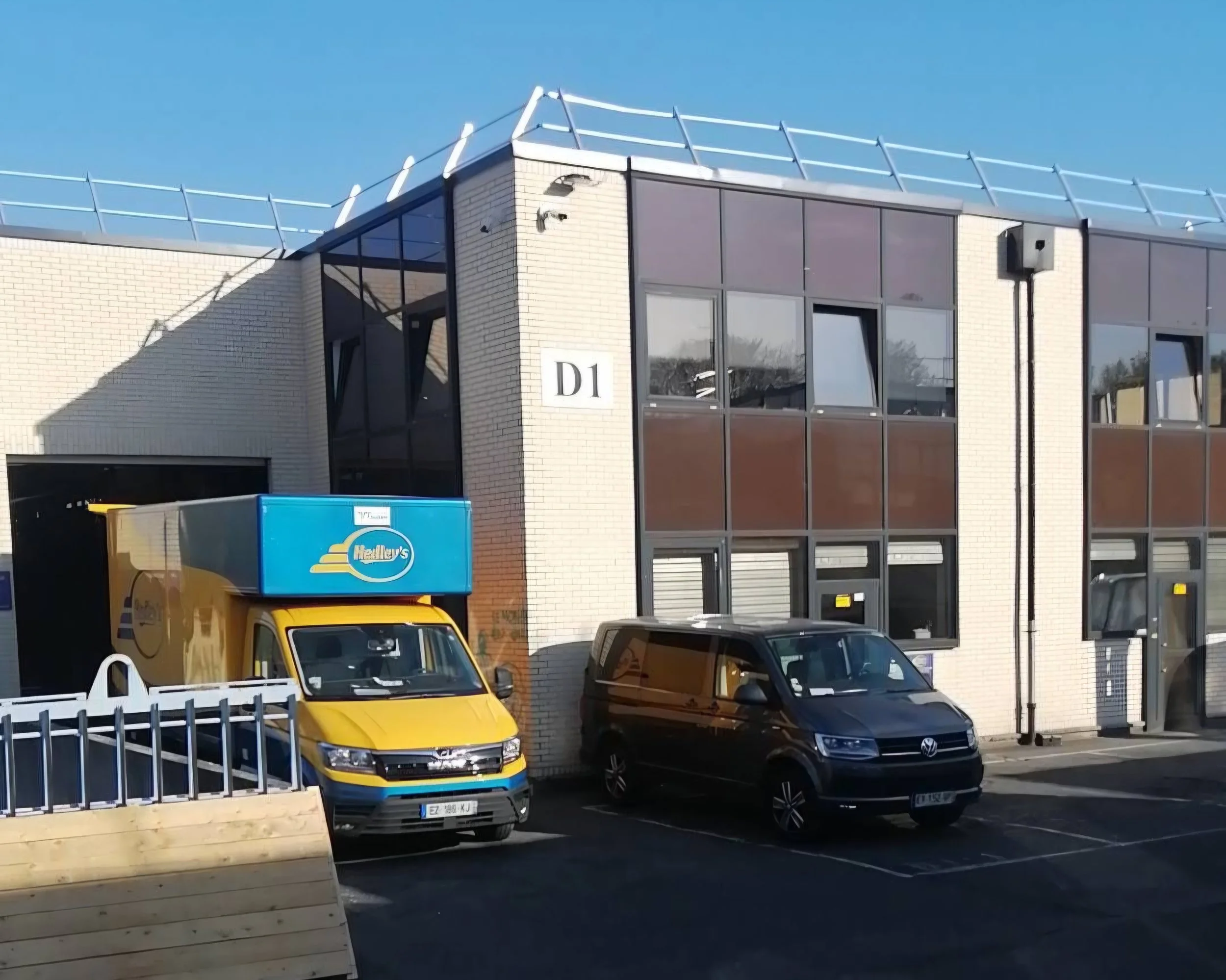 Bâtiment moderne avec deux véhicules stationnés devant, un camion jaune avec un logo