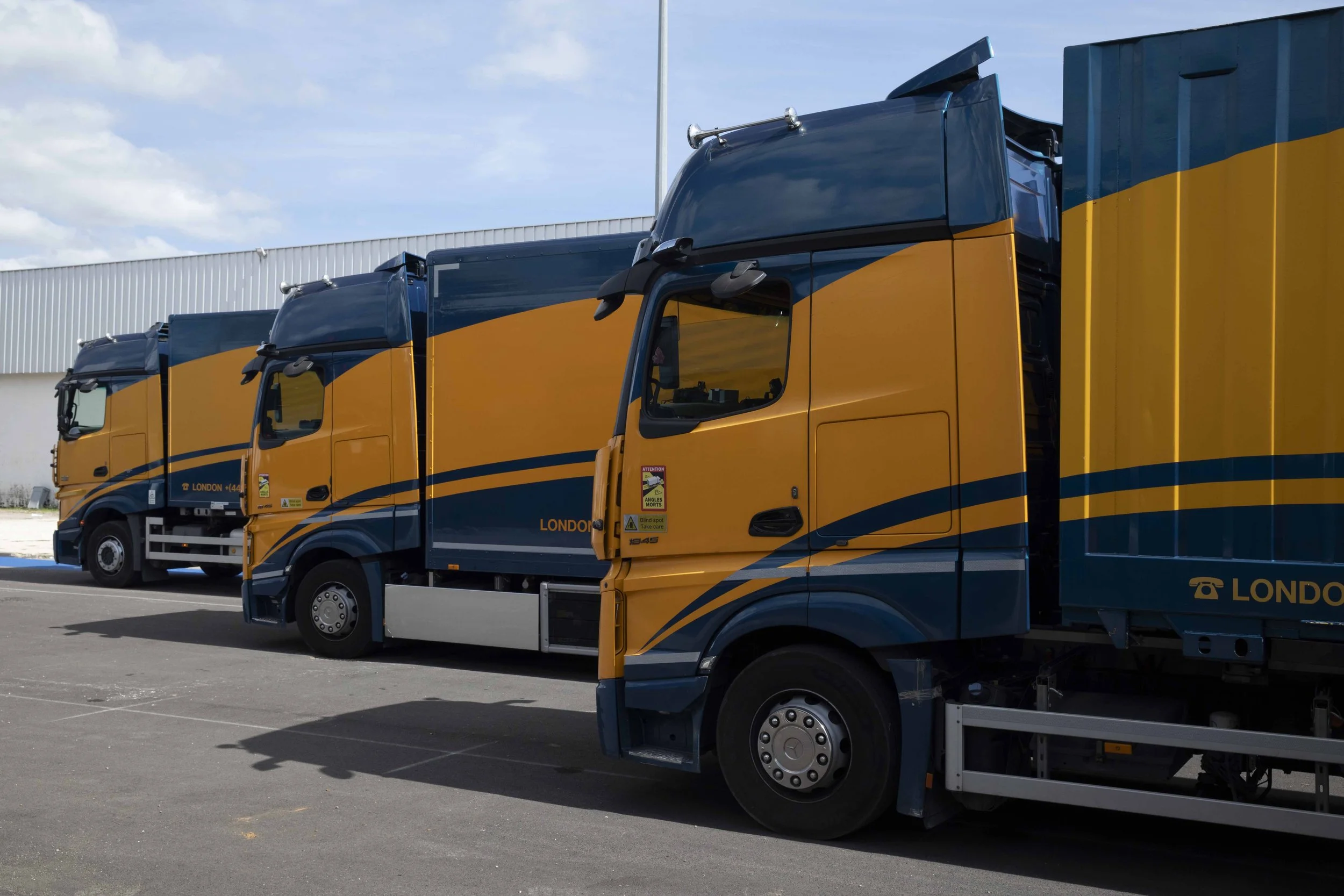 Three branding trucks parked in a lot in front of a warehouse building.