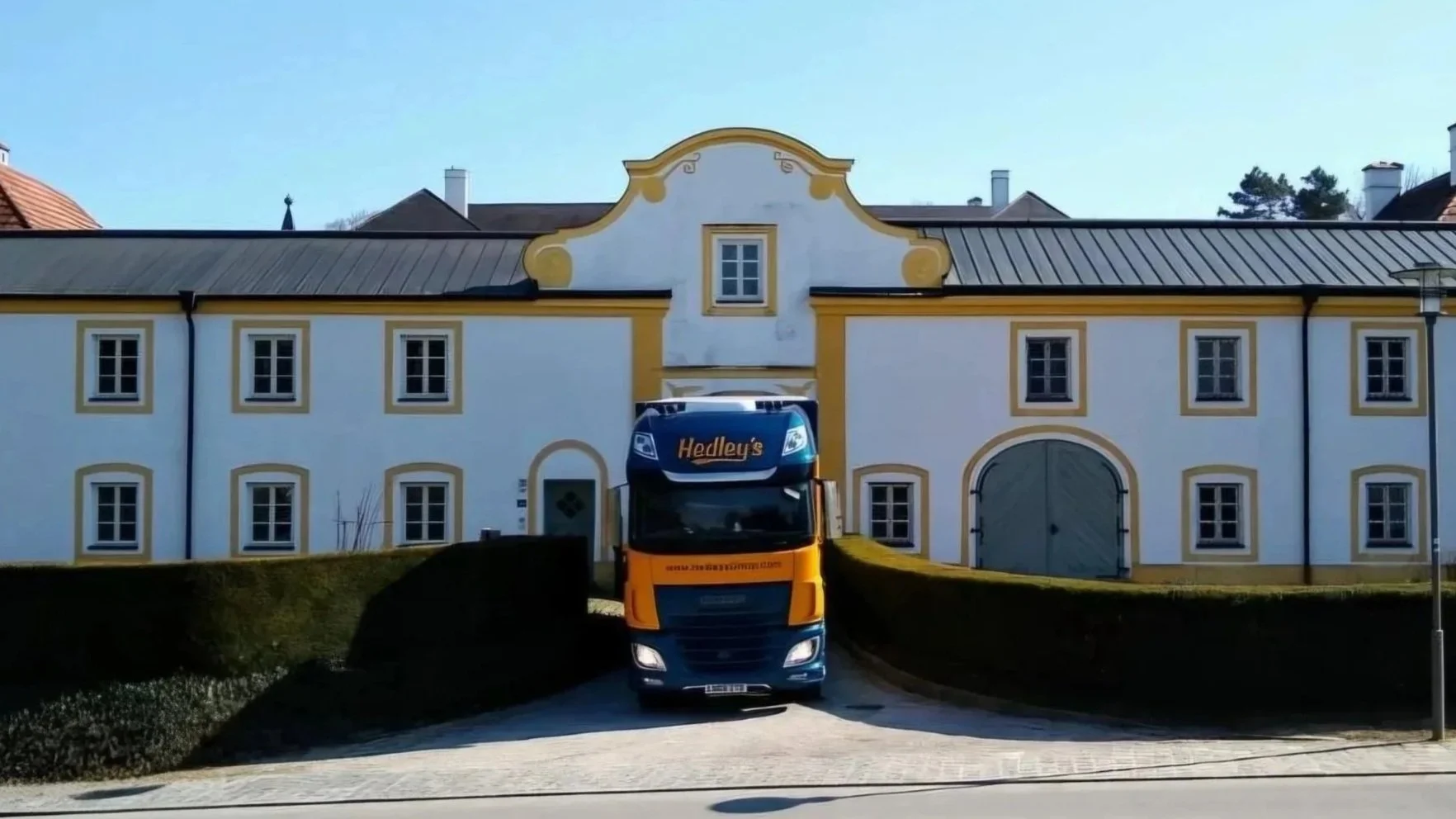 A large yellow and blue Hedley's delivery truck parked in front of a white building with yellow trim and several windows.