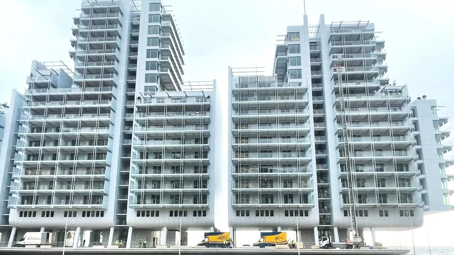 Immeuble en construction avec plusieurs étages et des balcons, des grues et des véhicules de construction en bas.