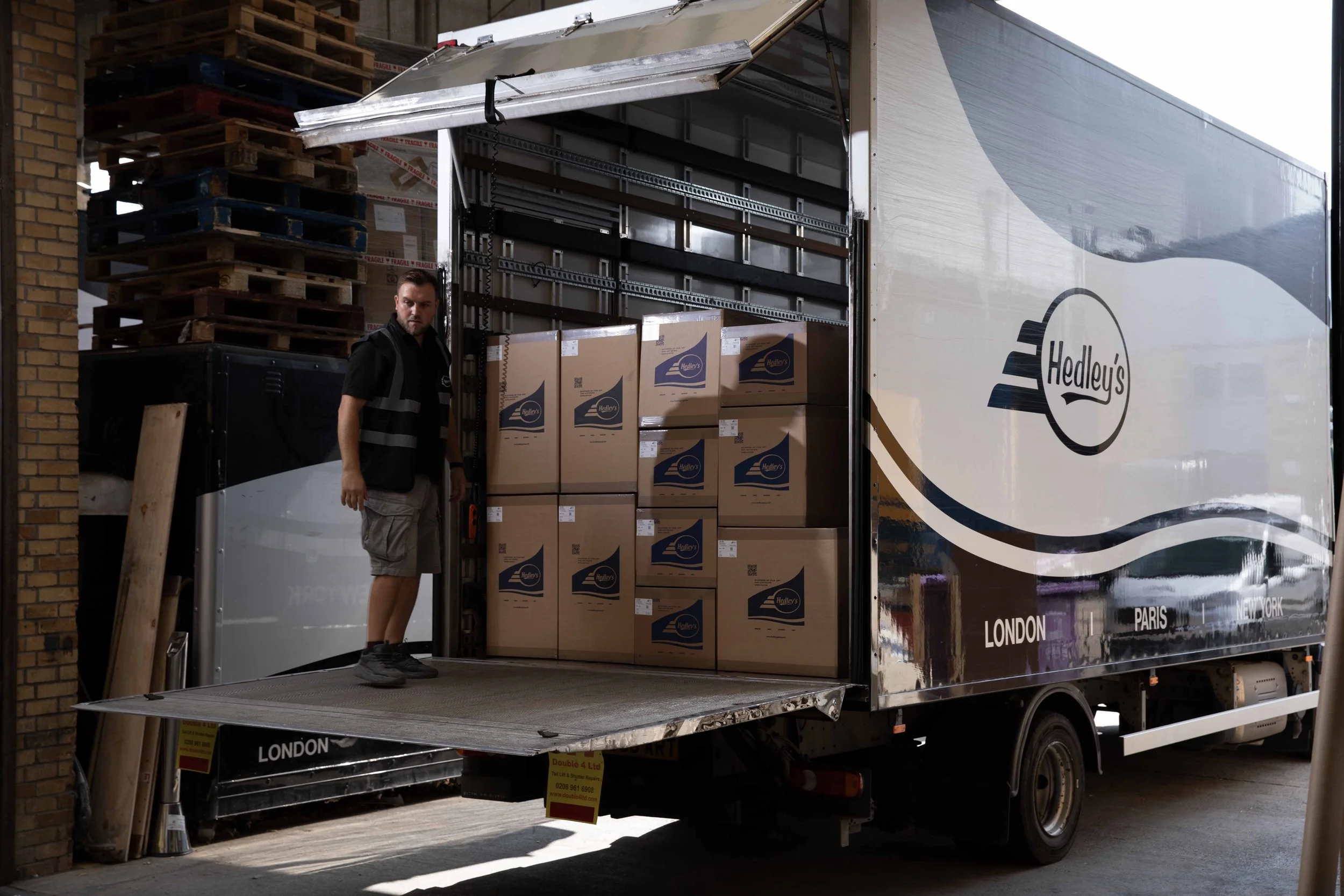 A man loading boxes into a Hedley's delivery truck parked outside a brick building.