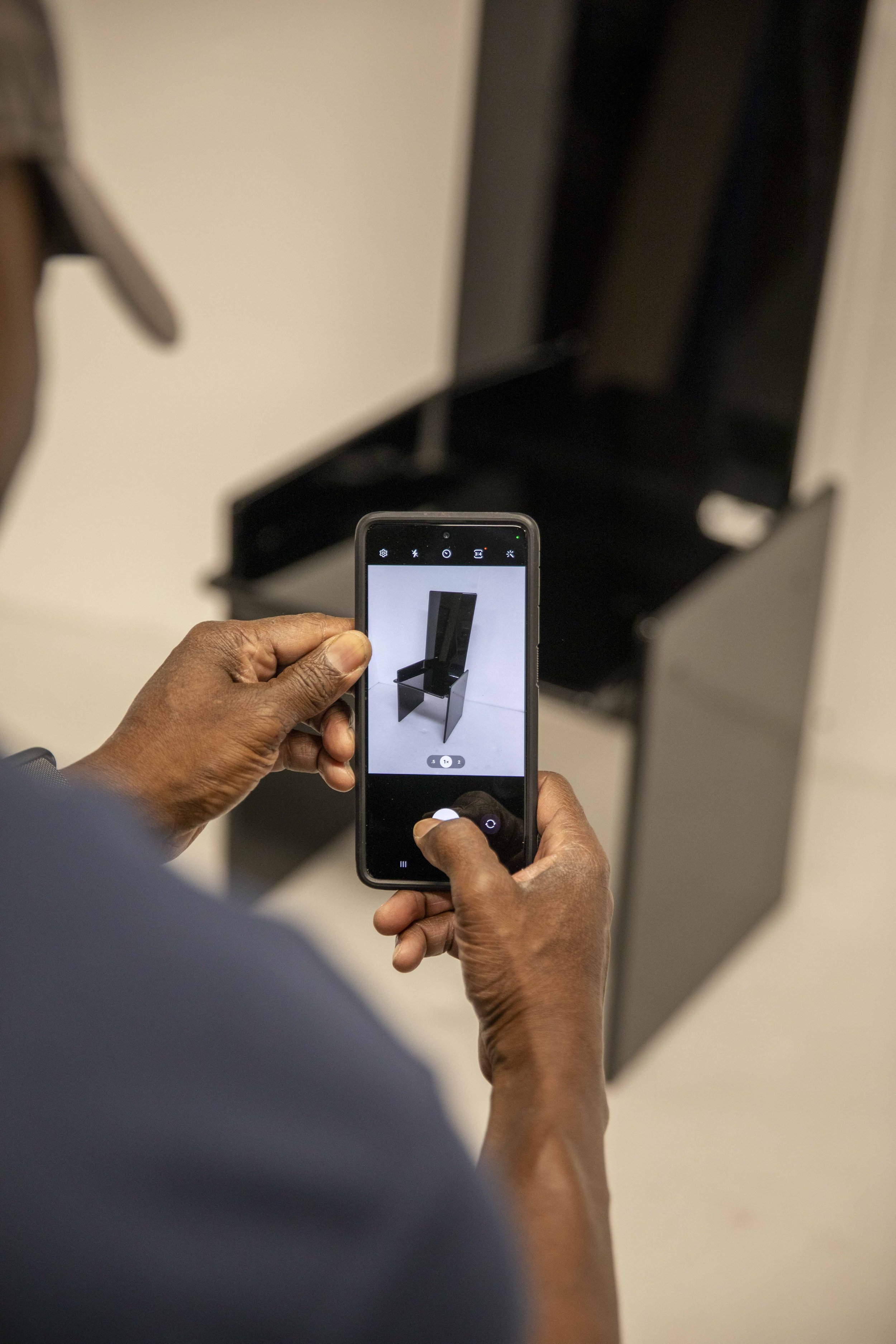 Person taking a photo of a black chair with their smartphone in an indoor setting.