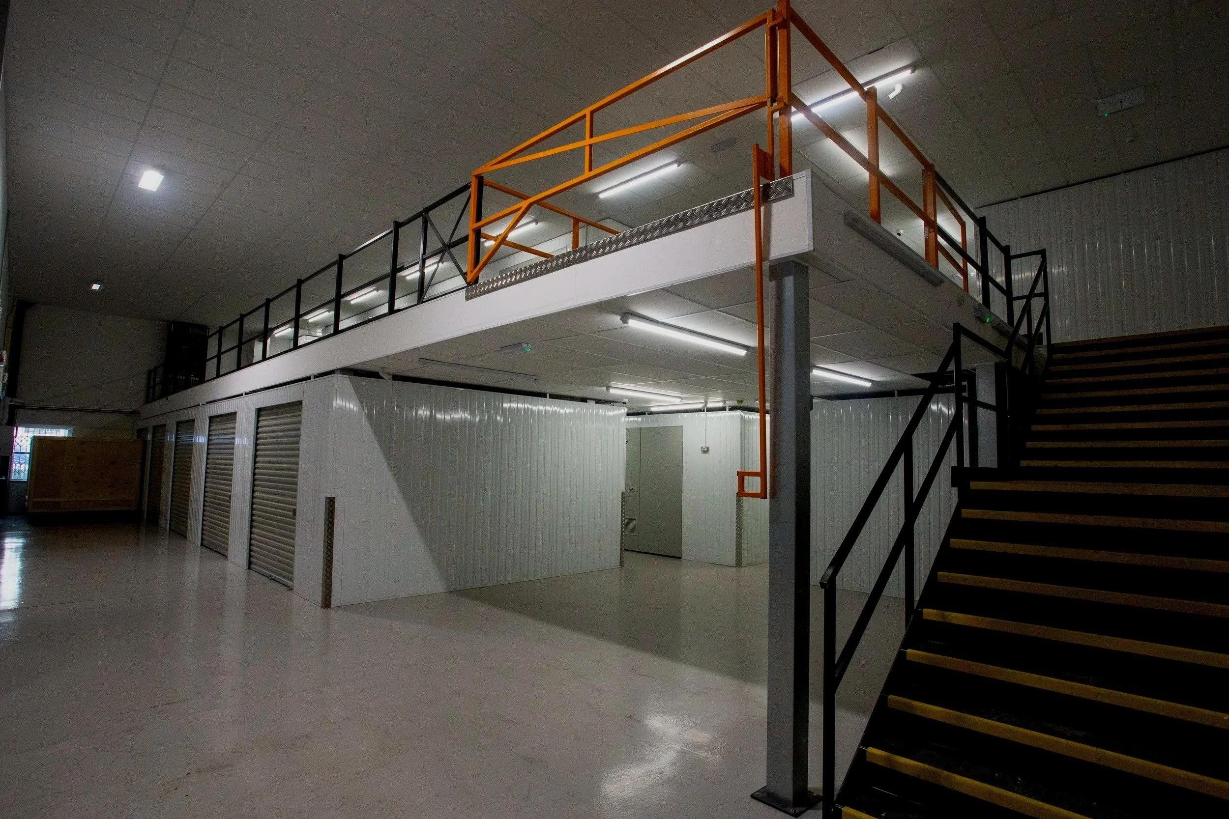 Empty industrial warehouse with metal stairs, upper level safety railing, and storage lockers.