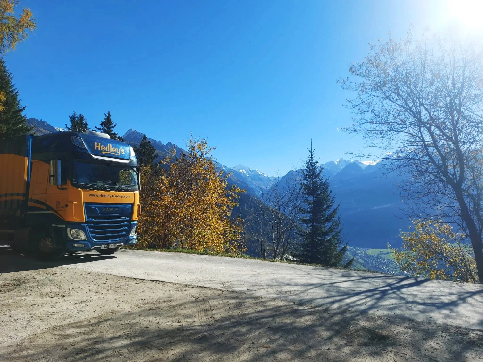 A Hedley's truck parked on a mountain road with a scenic view of mountains, trees, and a clear blue sky.
