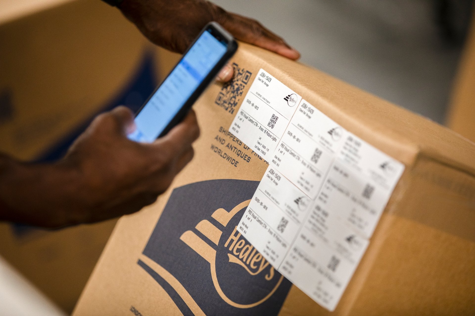 Une personne scanne un code QR avec son téléphone portable posé sur une grande boîte en carton avec l'étiquette d'expédition Sheplers Western Wear and Antiques.