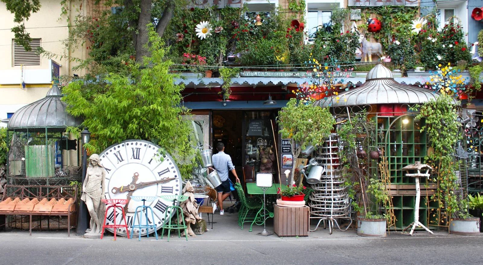 Colorful eclectic storefront with plants, a large clock, sculptures, and decorative items.