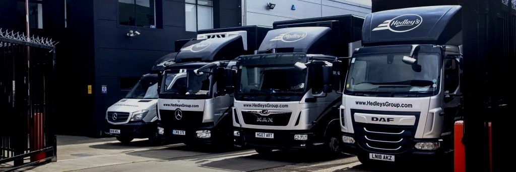 A row of delivery trucks parked outside a building with black walls.