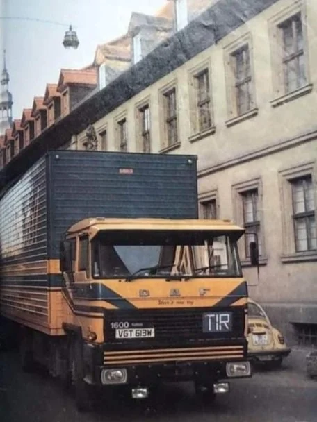 Yellow and black truck parked on a narrow city street with older buildings on the side.