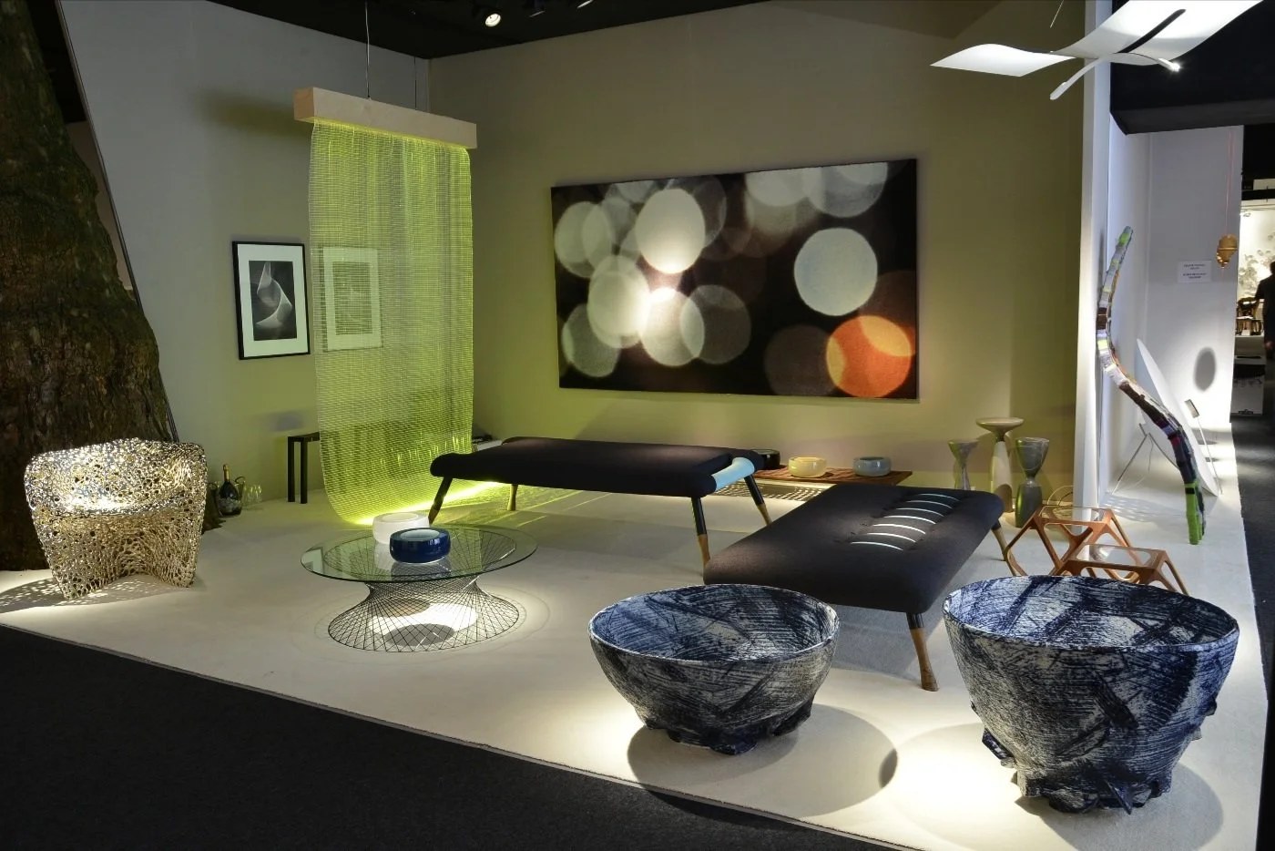 Modern living room display with black and gray furniture, decorative bowls, textured chairs, a large abstract art piece, and ambient lighting.