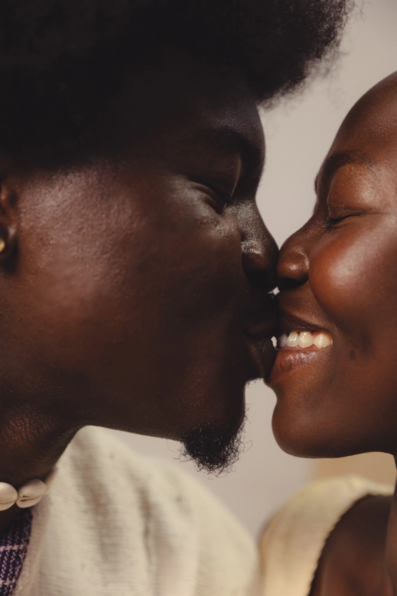 Two people with dark skin, close together, about to kiss, with smiles and their noses touching.