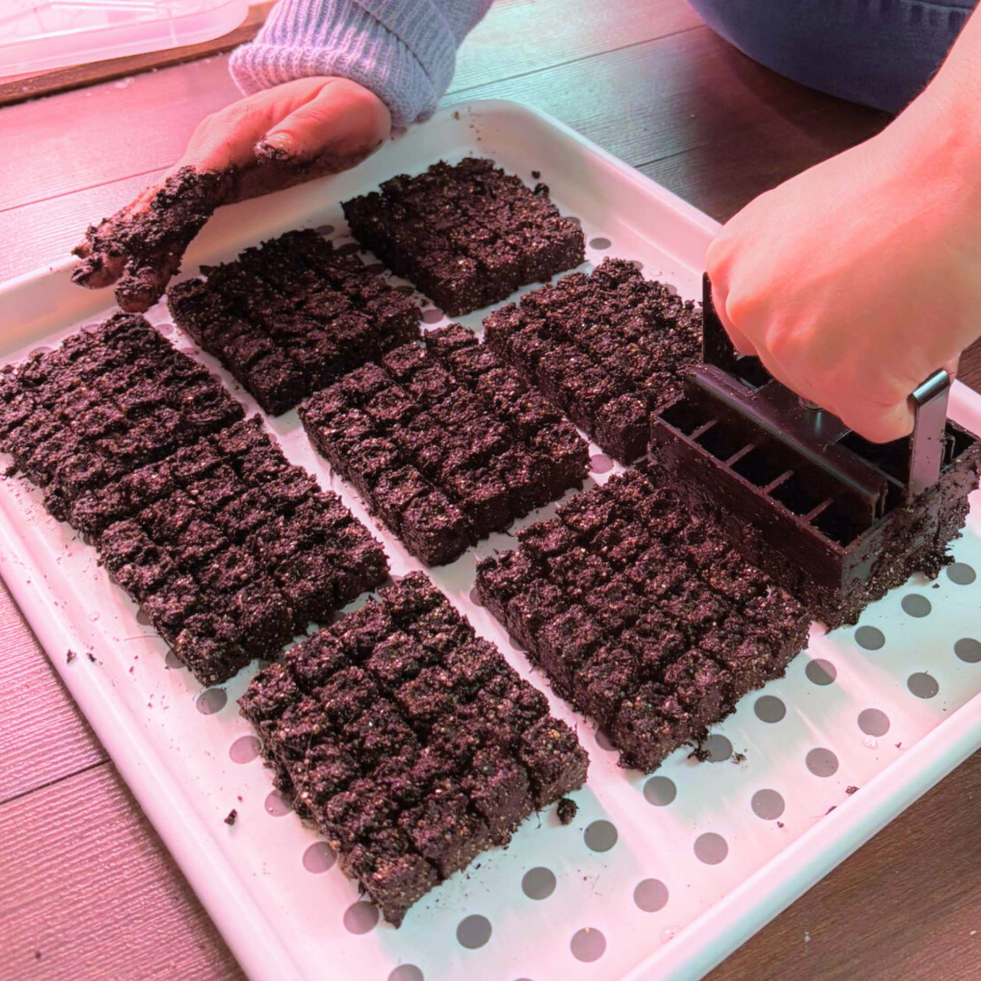 A person using a green cookie cutter to cut into a large batch of dark, crumbly brownie squares on a white tray with black polka dots.
