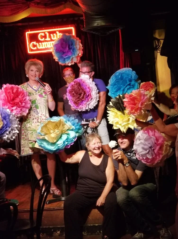 Brini Maxwell on stage with regular attendees at Club Cumming's Make It with Brini event holding up the paper flowers they made during the event.