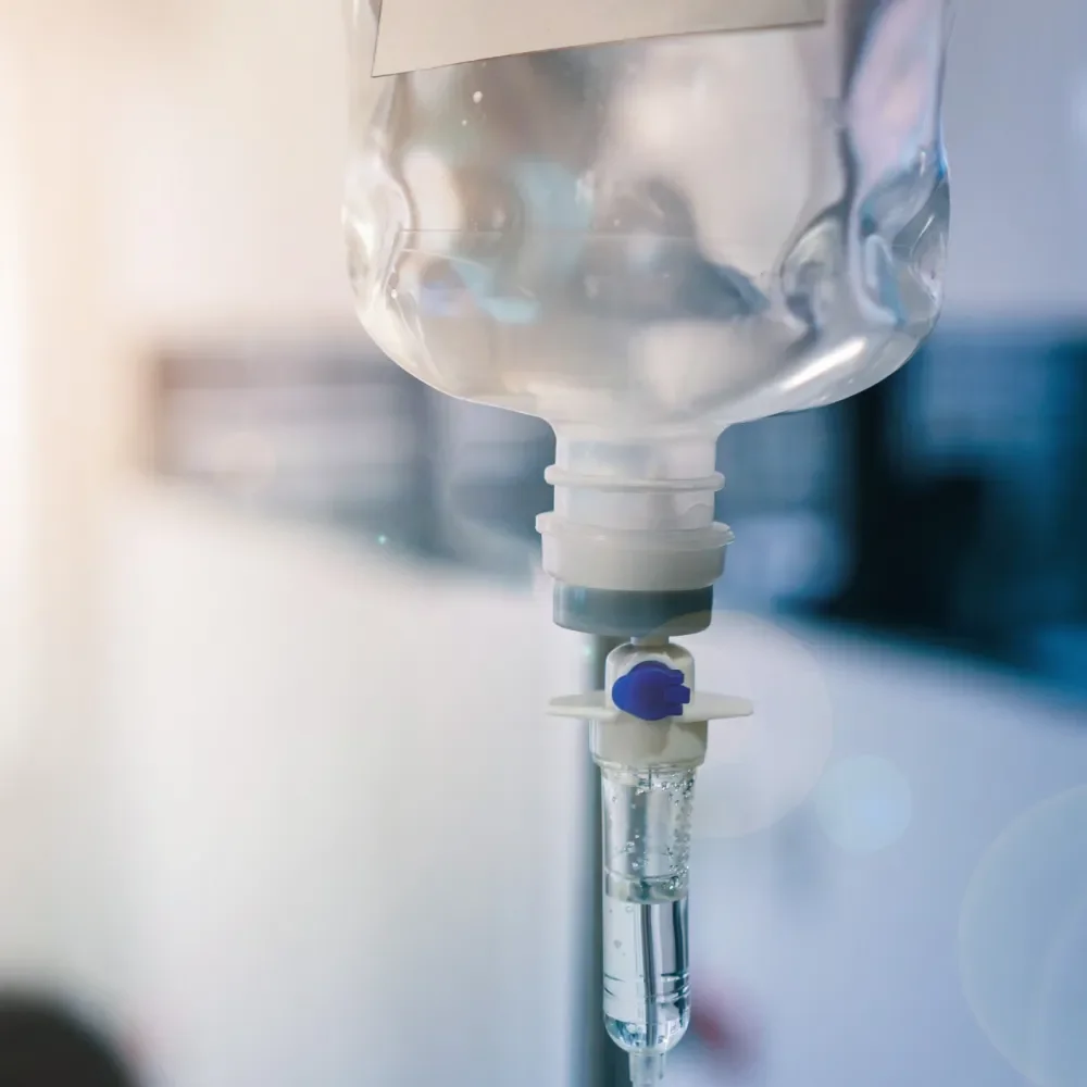 Close-up of a hospital IV drip bag hanging with a needle and tubing hanging from it.
