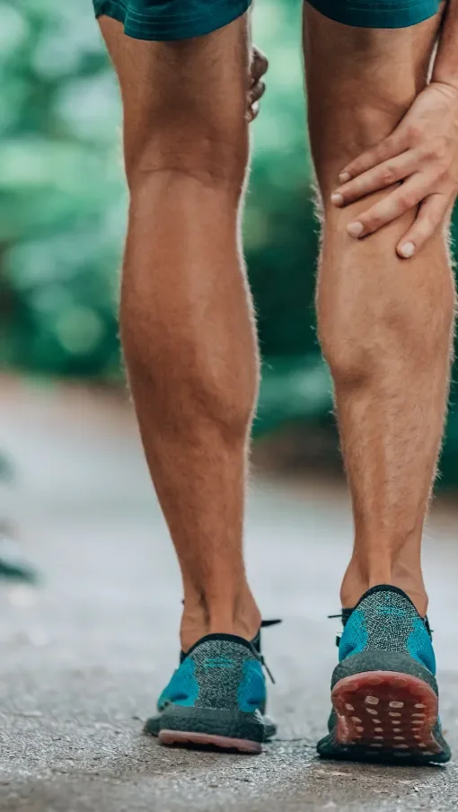 A person wearing running shoes, with one hand on their leg, walking outdoors on a paved path.