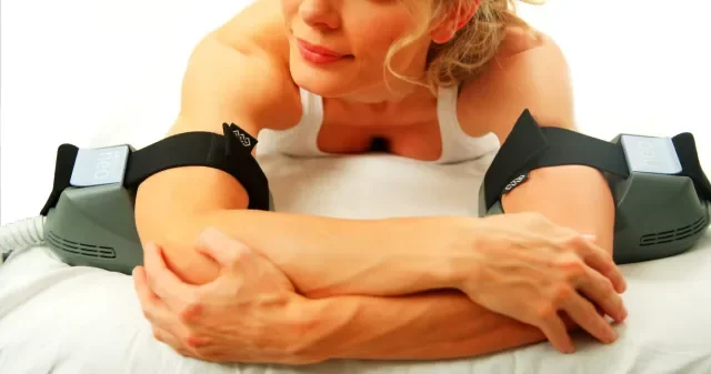 A woman lying on her stomach with her head resting on her hand, wearing stereo exercise bands on her arms.
