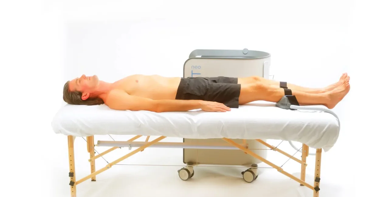 A person lying on a medical examination table with a device placed on their legs, likely for a diagnostic or therapeutic procedure.