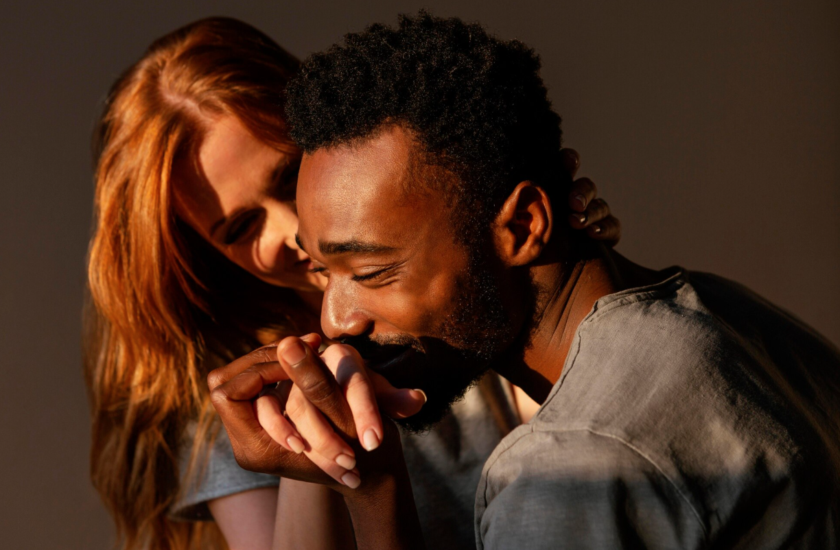 A man and woman share a moment of affection, with the woman gently touching the man's face and both smiling softly.