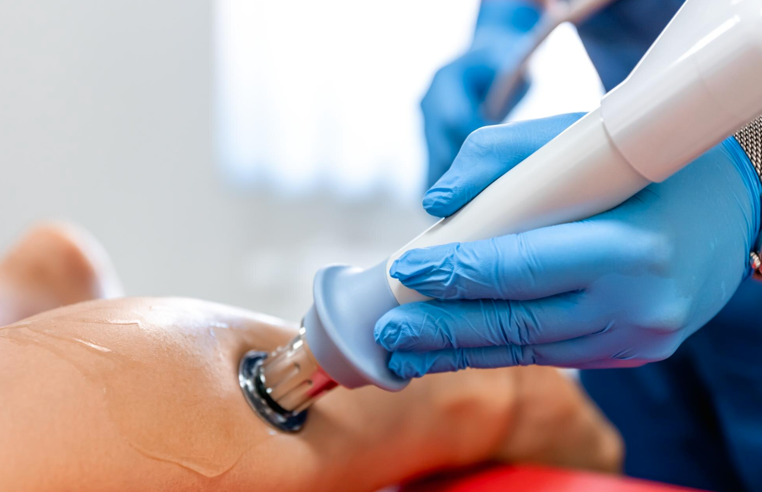 A medical professional in blue gloves uses a handheld ultrasound probe on a patient's abdomen during a medical examination.