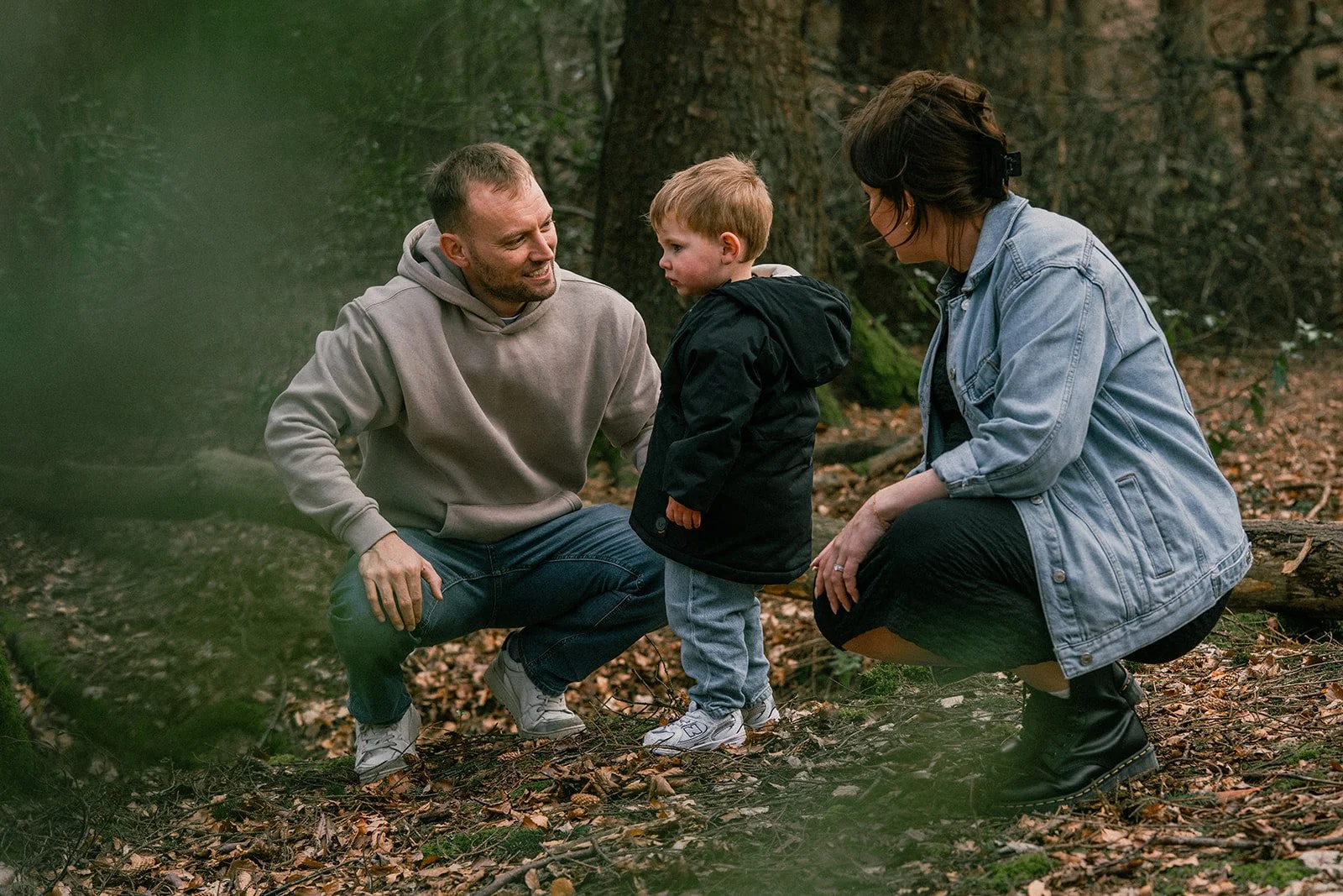 A family of three in a forest, with a man and woman crouching down to talk to a young child.