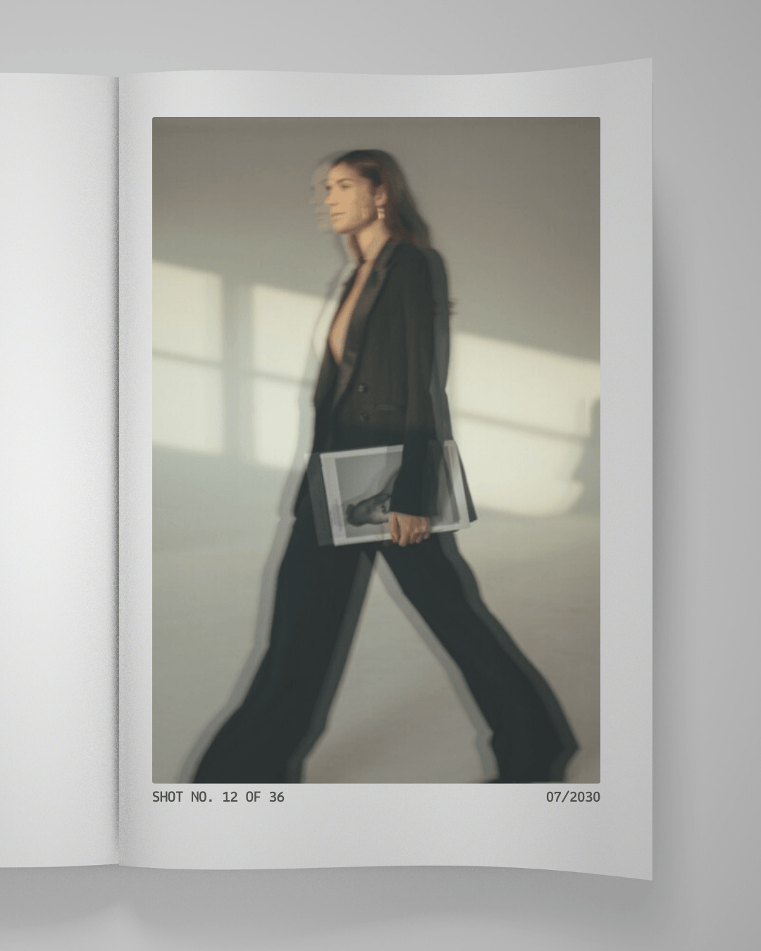 Blurred image of a woman in black pants and blazer walking while holding a magazine.