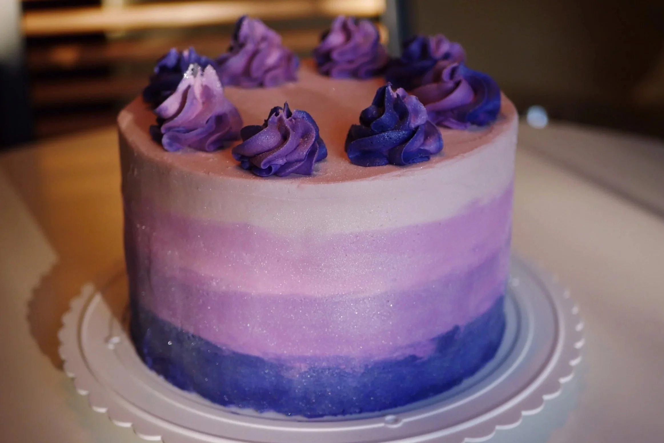 A multi-layered cake with purple and pink marbled frosting topped with purple buttercream flowers.