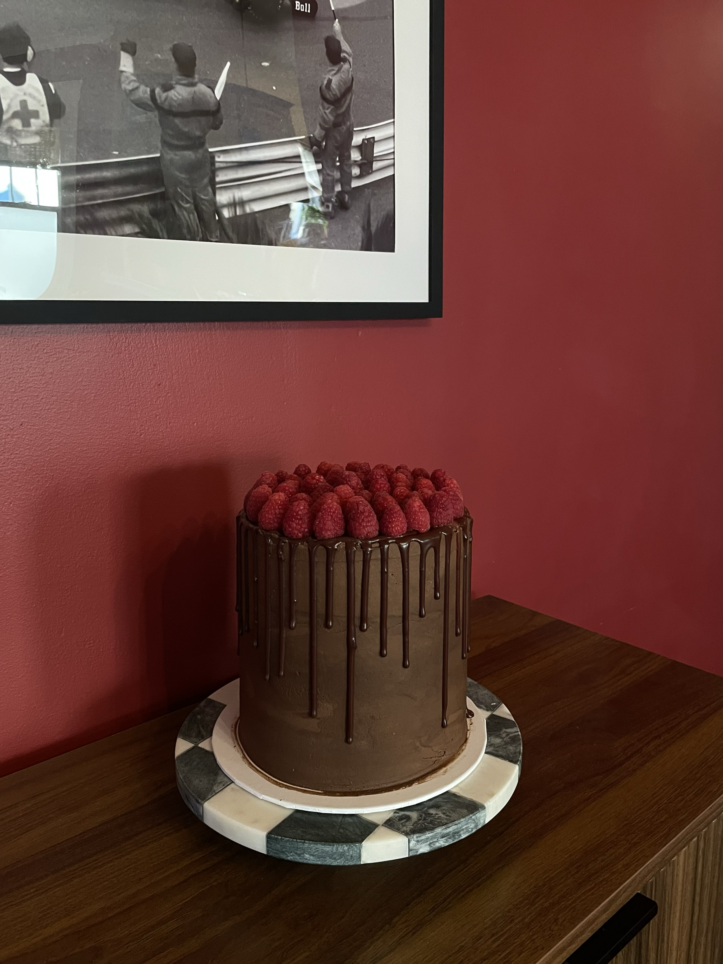 Chocolate layered cake topped with raspberries and drizzled with chocolate ganache on a marble cake board.
