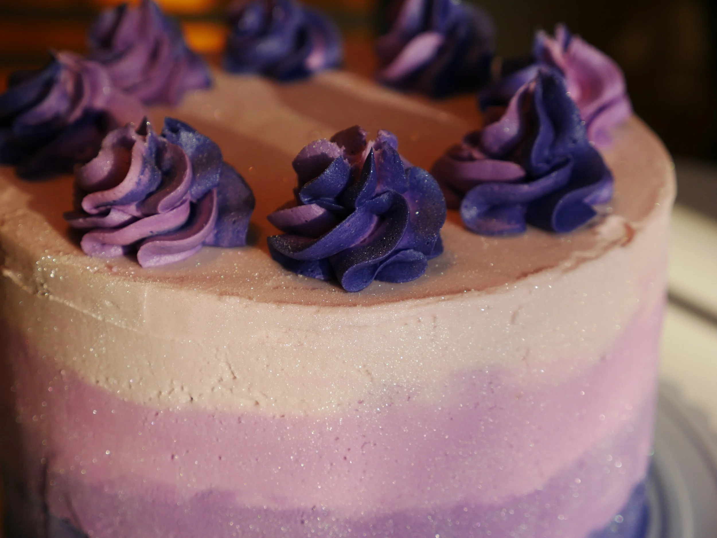 Close-up of a two-tone pink and purple decorated birthday cake with purple frosting rosettes on top.