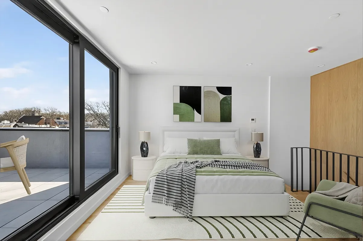 Modern bedroom with white bed, black and white striped blanket, green pillow, two black lamps, abstract wall art, sliding glass door leading to balcony, green chair, and wooden wall panel.