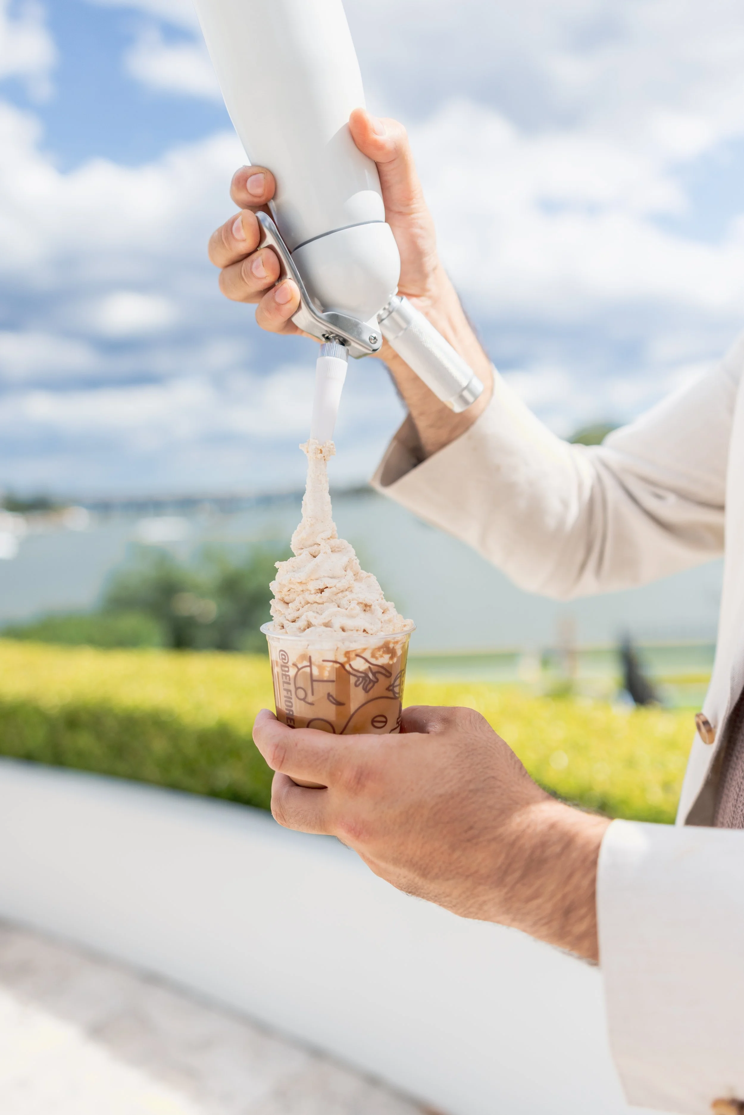 Person holding a cup of ice cream while dispensing soft serve ice cream from a machine outdoors.