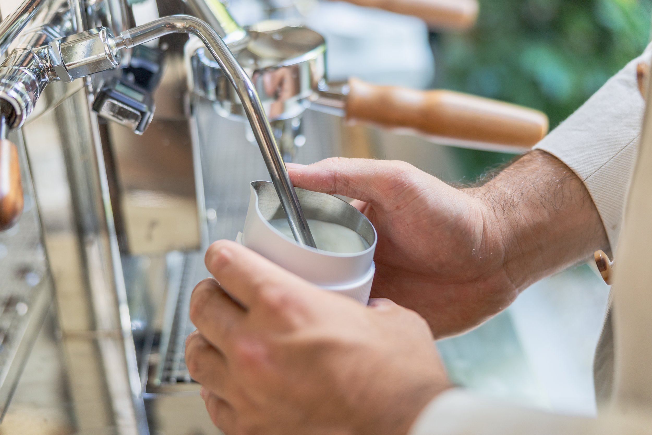 Person filling a cup with milk from a coffee machine in a cafe or coffee shop.