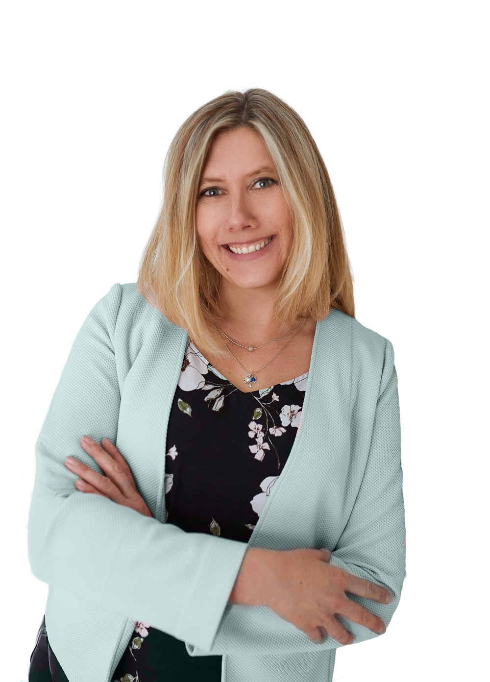 Keri Schwebius with blonde hair smiling, wearing a light blue blazer over a black floral dress, standing with arms crossed.