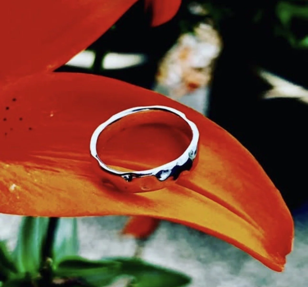 A silver ring resting on an orange flower petal with some water droplets on it.