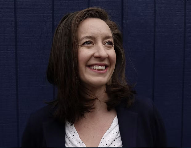 Smiling image of Elena K. Abbott in white polka dots blouse and blue blazer against a navy blue background
