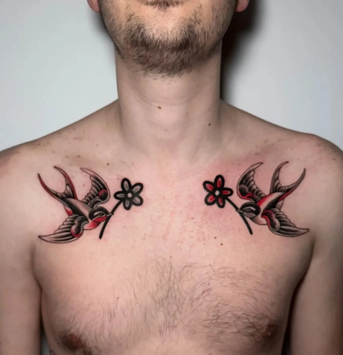 A shirtless man with tattoos on his chest and arms, including two swallows with flowers and a '1998' tattoo.