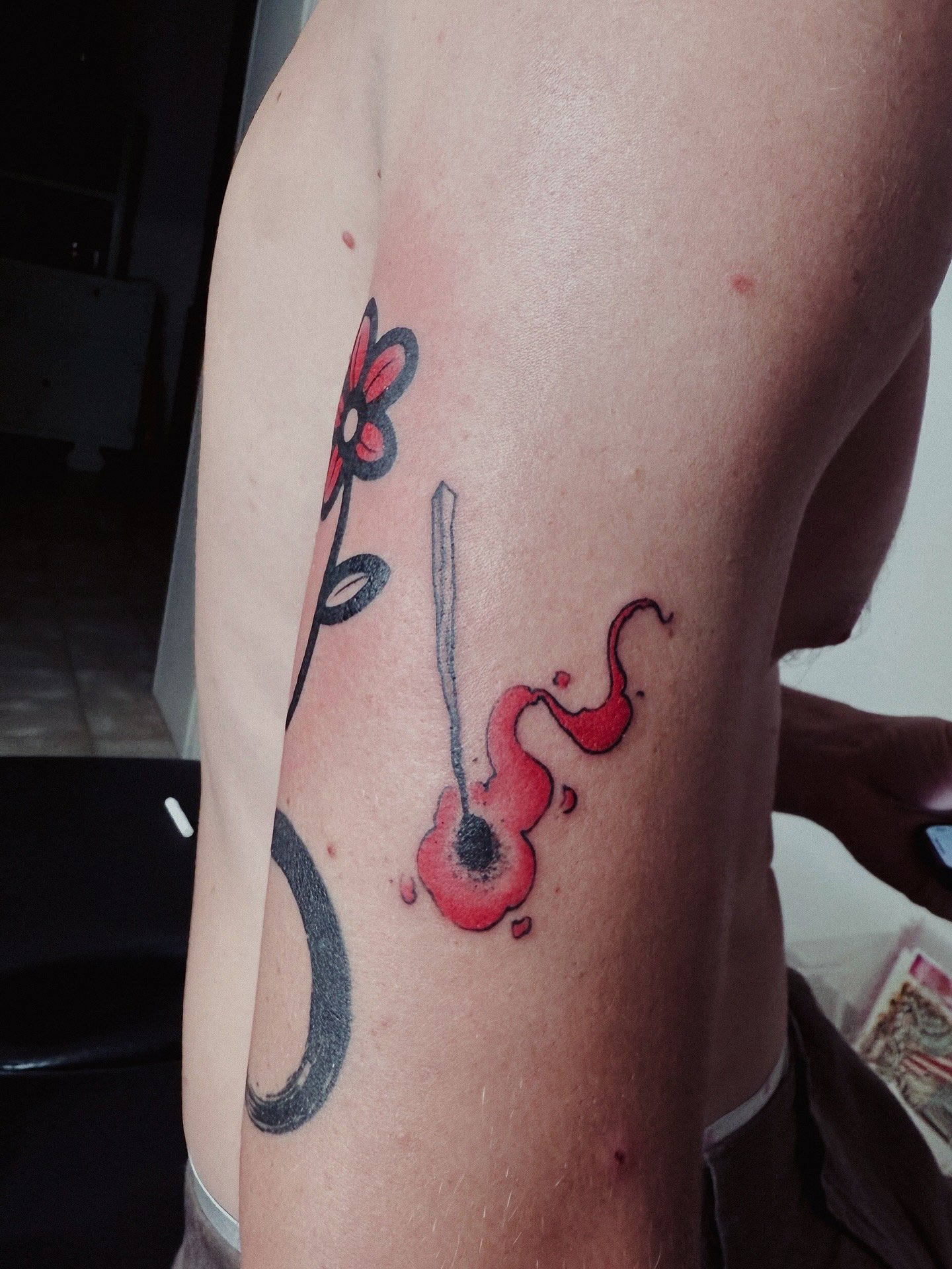 Tattoo of a red and black flower with a stem and an abstract red splash on a person's side ribcage.