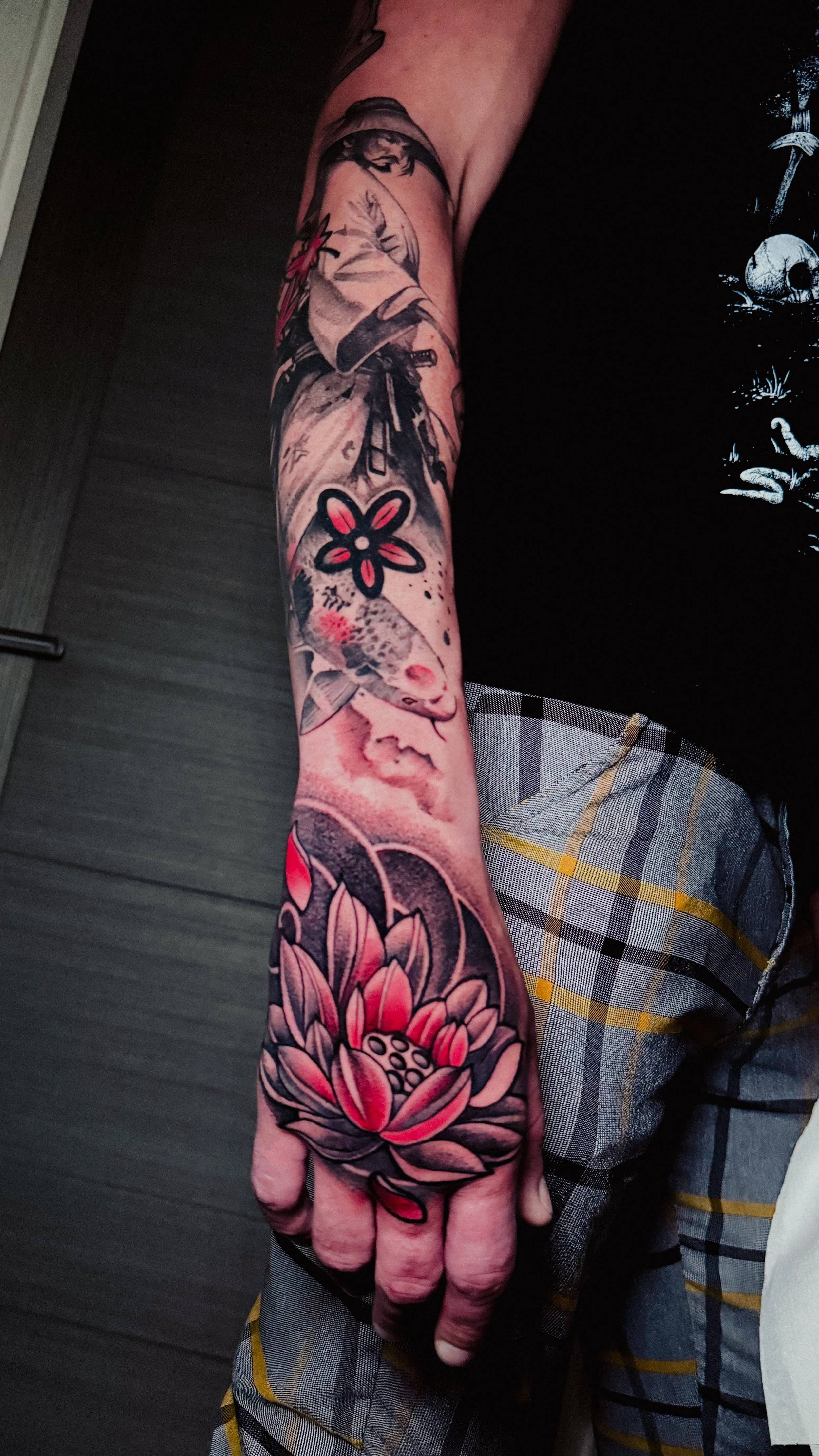 Tattooed arm featuring a large pink lotus flower on the hand, a fish, and a flower on the forearm.