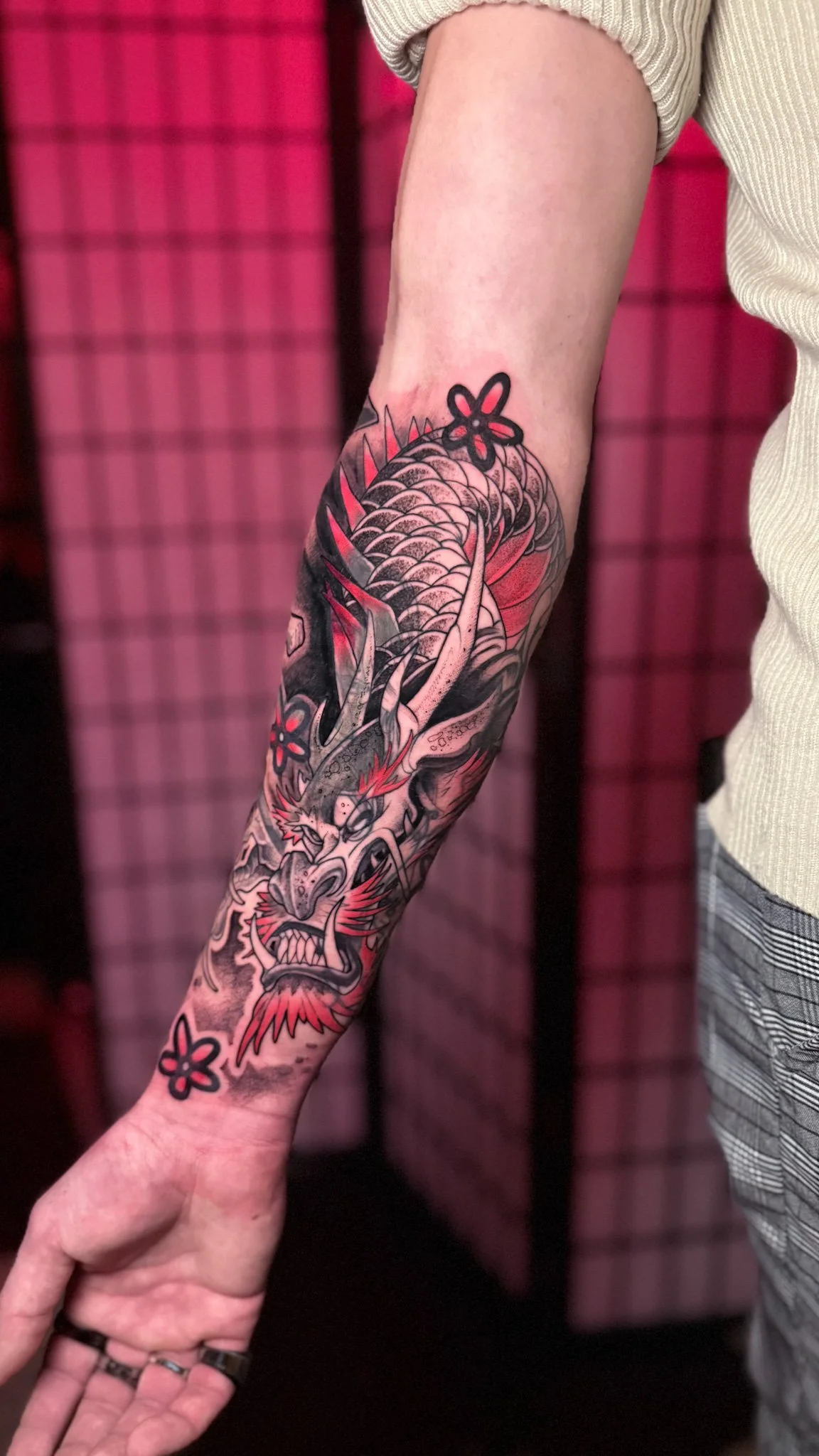 Tattoo of a fierce dragon with red accents and flowers on a person's arm.