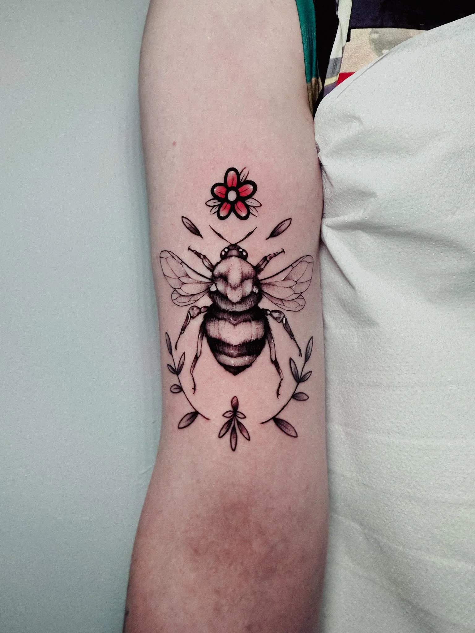 Tattoo of a bee with floral and leaf elements on a person's forearm.