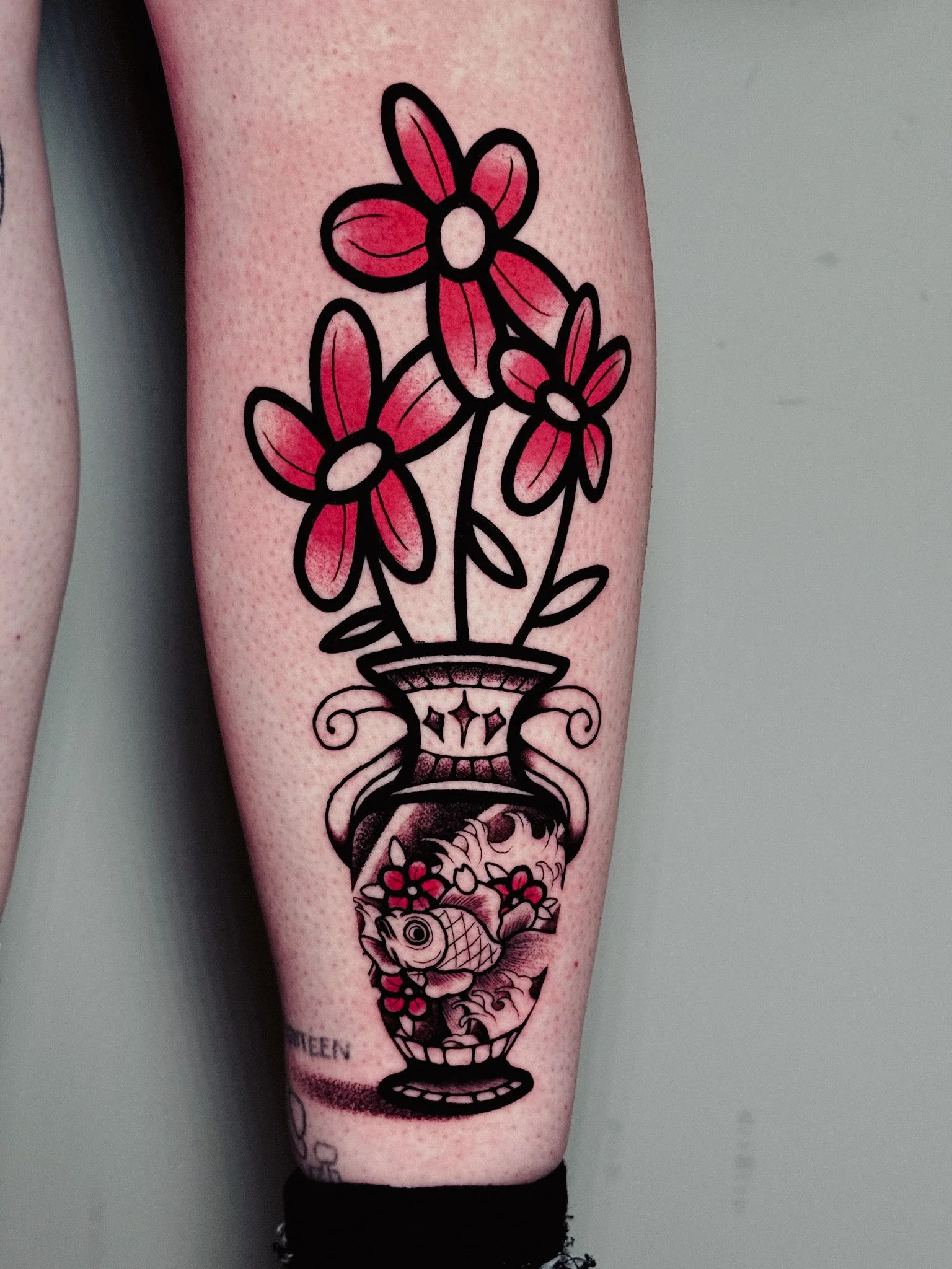 Tattoo on person's arm depicting a vase with pink flowers and a goldfish inside.