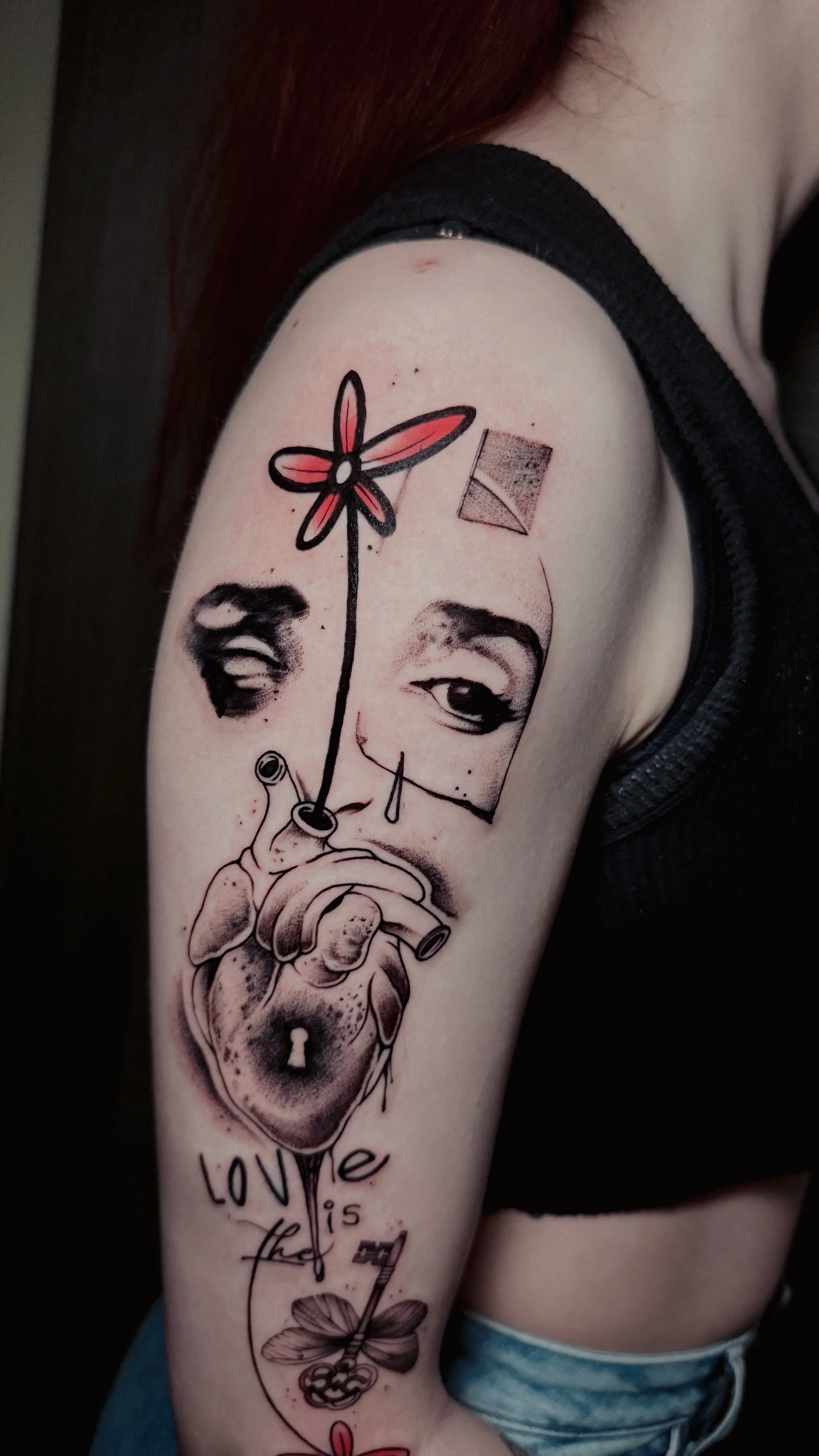 Tattoo of a woman's face with one eye closed and an expression, holding a heart-shaped lock and a key, with a flower on a stem coming from her eye to the lock, and the words "love" and "is the" with a key and flower below.
