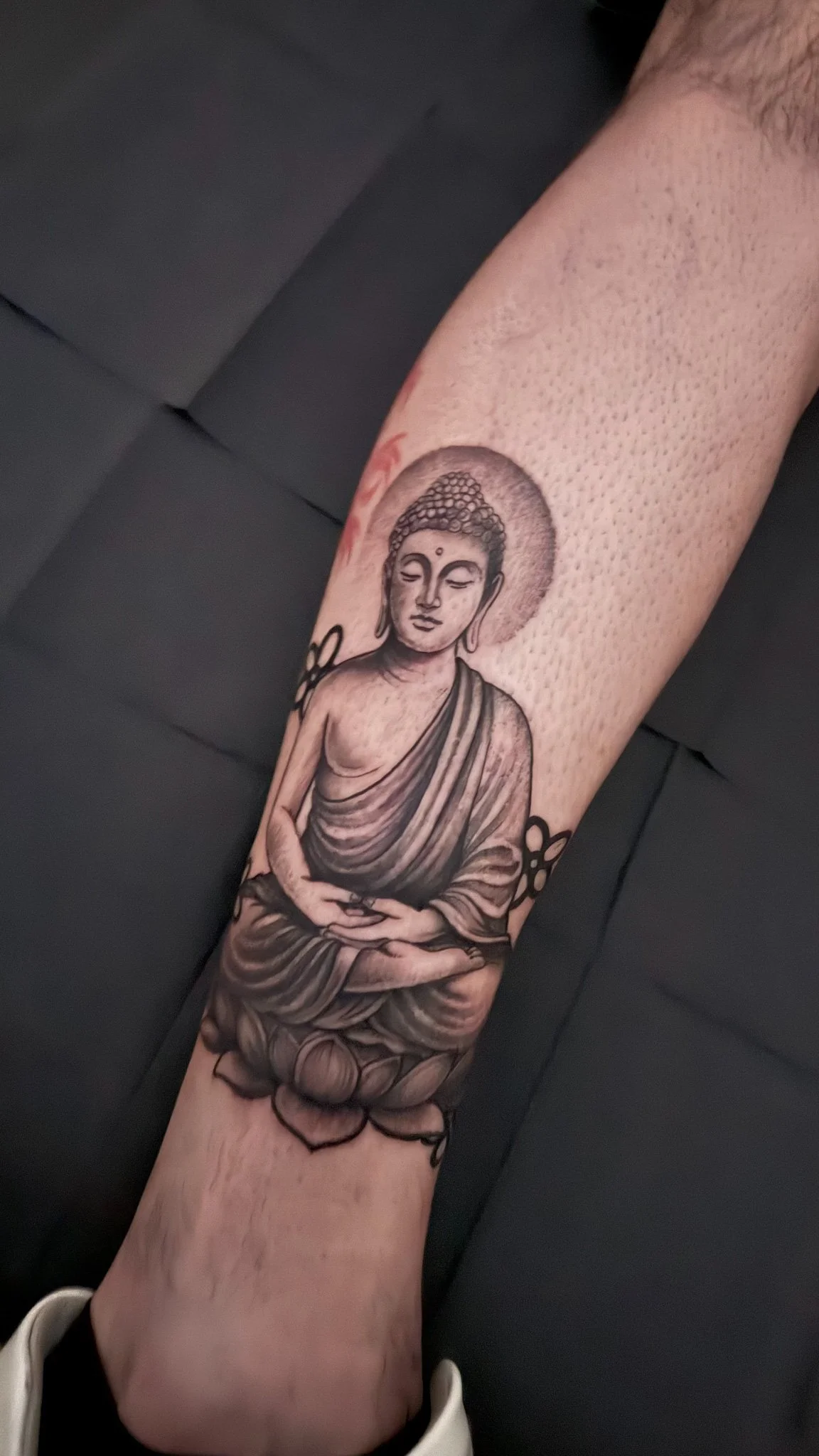 Black and gray tattoo of Buddha in a meditative pose on a person's forearm.