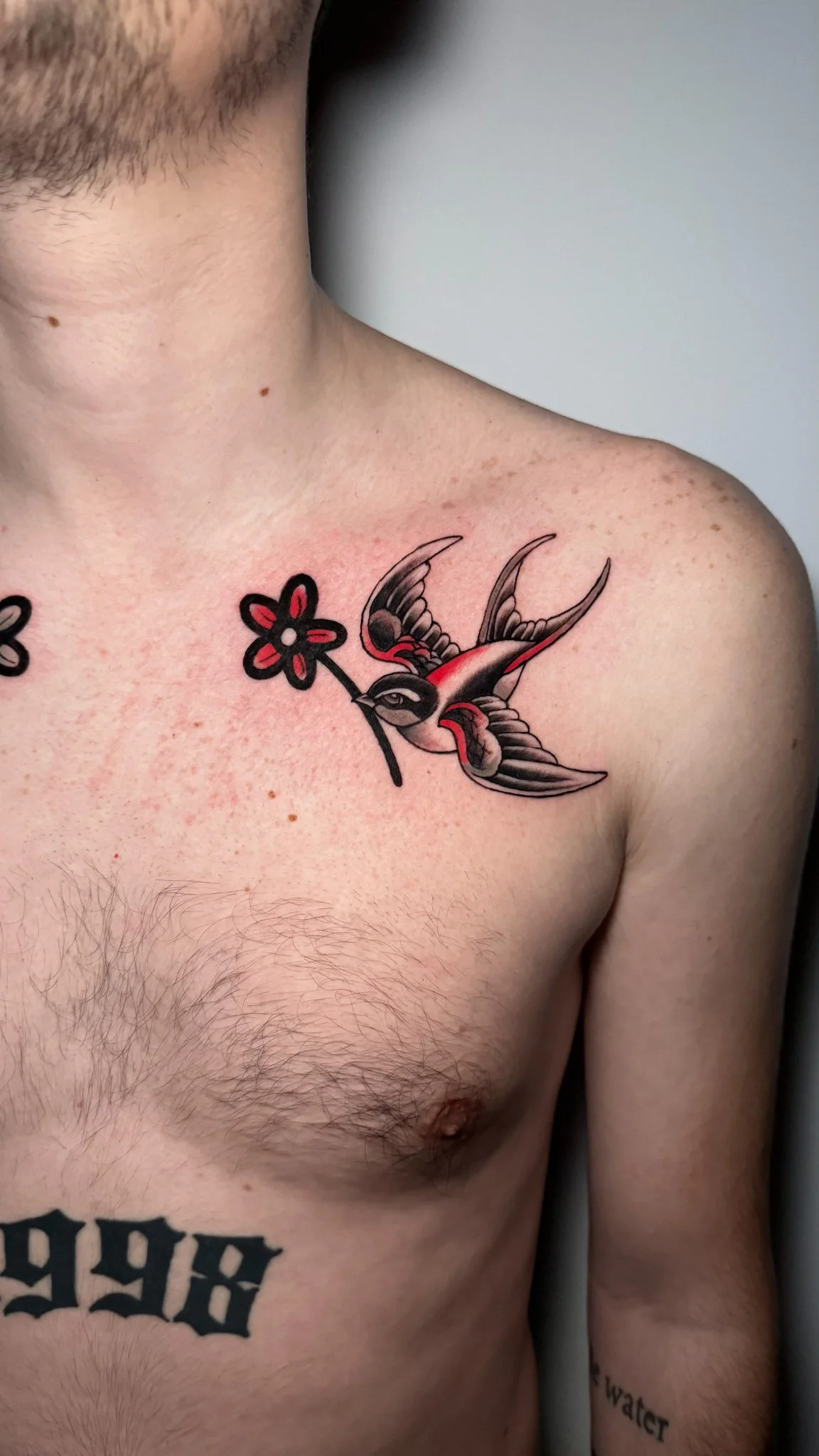 Tattoo of a swallow holding a flower on a man's upper chest.