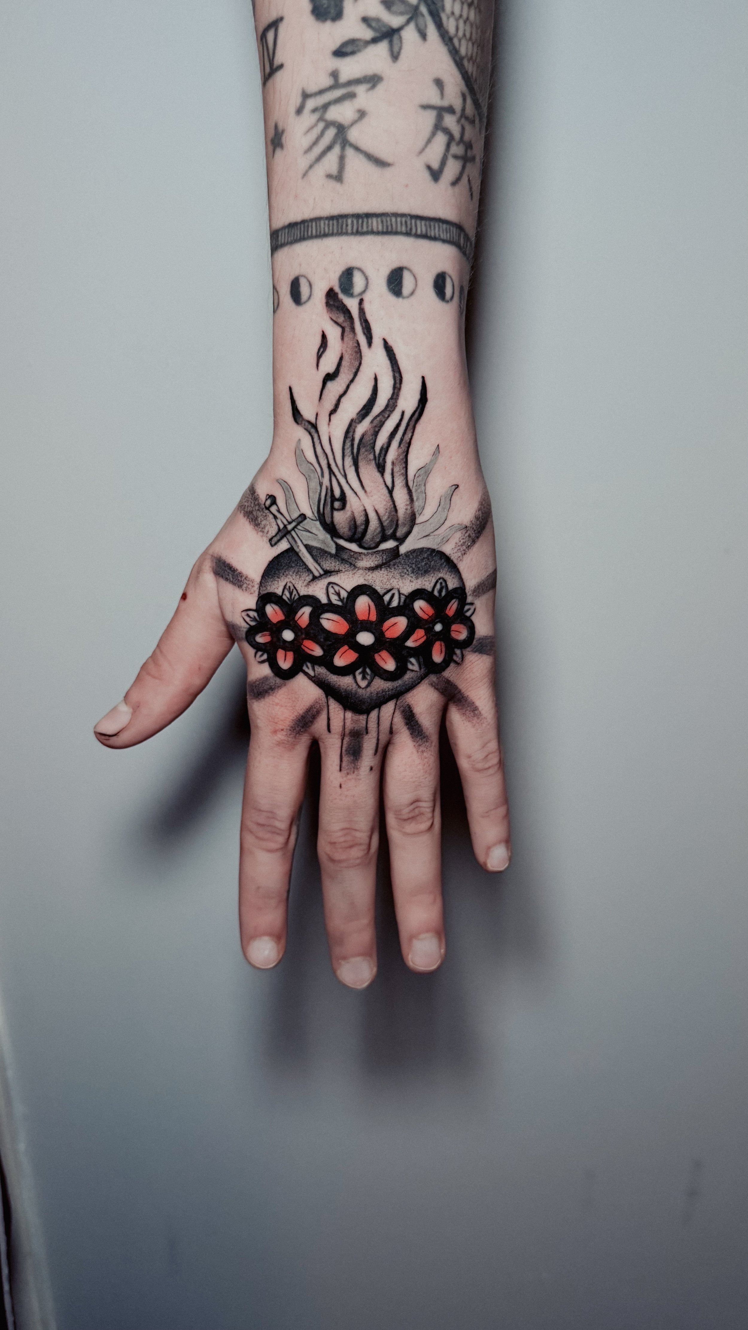 Tattoo of a flaming heart with flowers, a sword, and a Band-Aid on the hand